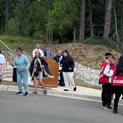 Photo of ceremonial totem pole waking with singing and dancing.