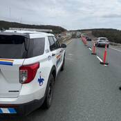 A fully marked RCMP police vehicle sits inside a highway construction zone, while vehicles pass in the right-hand lane. Construction crews are visible in the background.