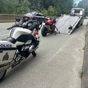 A red sport motorcycle is loaded onto a tow truck on Highway #99 as a BC Highway Patrol motorcycle is parked in the foreground