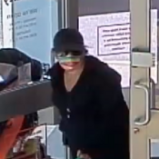 Female in dark clothing with a hat and sunglasses carrying a green bag.
