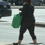 Female, viewed from behind, wearing dark clothing and carrying a green bag.