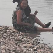 Karen Tessier sitting in the water wearing a black and white patterned dress with a small black dog.