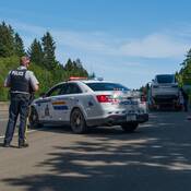A BC Highway Patrol officer supervises in front of his police car while a Tesla is loaded onto a tow truck