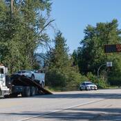 A white sedan is loaded onto a tow truck as a BC Highway Patrol cruiser sits parked under a road sign that says “don’t drink and drive”