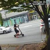 Police Body Worn Camera image that shows a small youth wearing shorts, a T-shirt and an oversized helmet and shoes operating an E Scooter in heavy traffic