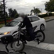 An uninsured electric motorcycle and its rider who fled from police. The rider is a young, skinny male with brown skin and a receding chin wearing all black clothing and a white bicycle helmet