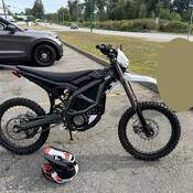 An e-dirt bike parked beside an unmarked police vehicle and a helmet in a parking lot.