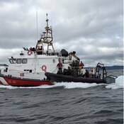 A large Canada Coast Guard vessel and a RCMP Zodiac vessel travel side by side on the water.