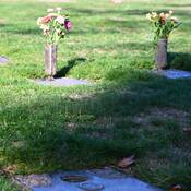 Three grave markers, two with bronze vases and flowers, one with an empty hole where the vase used to sit.