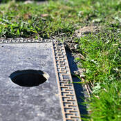 An empty hole on a grave marker where a vase used to sit and another grave marker in the background.