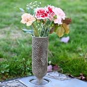 A bronze vase with flowers in it on a grave marker.