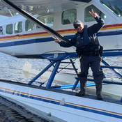Constable Darren Maizis standing on the RCMP Float Plane on the shore of a remote lake in the Skeena Region