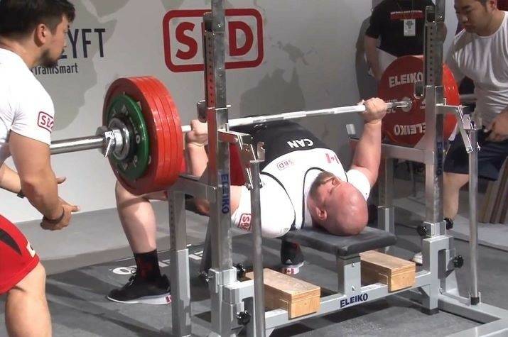 A man lays on a weight bench, holding a bar with large weights on each end.