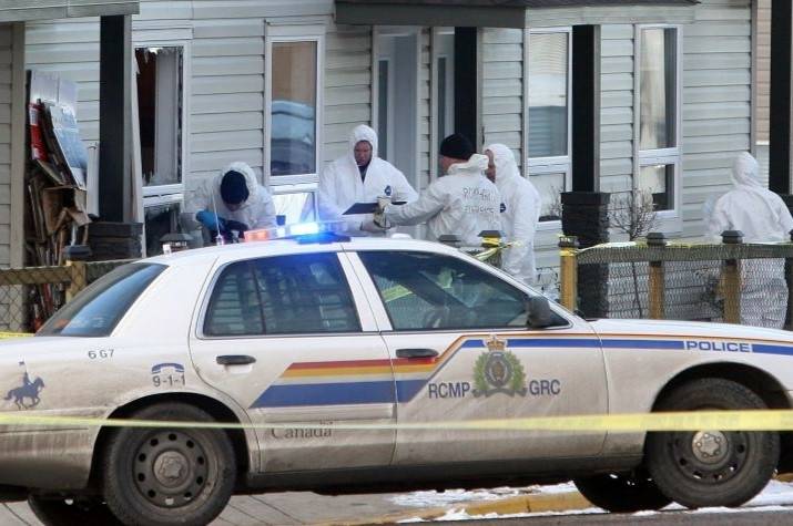RCMP specialists wearing white protective suits work outside a damaged home. An RCMP cruiser is parked nearby.