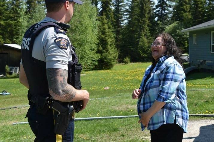 A male RCMP officer and an Indigenous woman face each other smiling in a treed yard next to a small blue house.