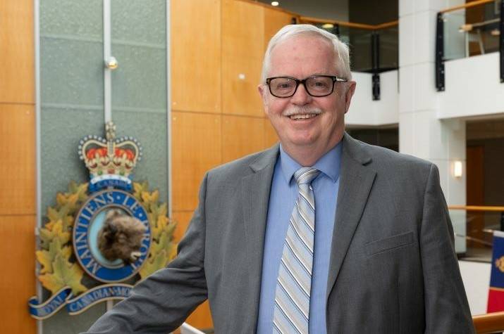 Man wearing suit stands in corporate building. A large RCMP crest is mounted to the wall behind him.