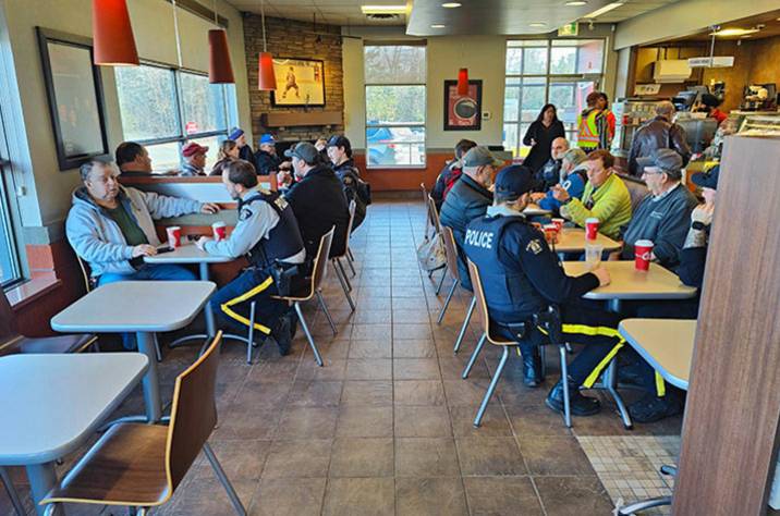 Uniformed RCMP officers and civilians are seen sitting down at tables in a Tim Horton’s.