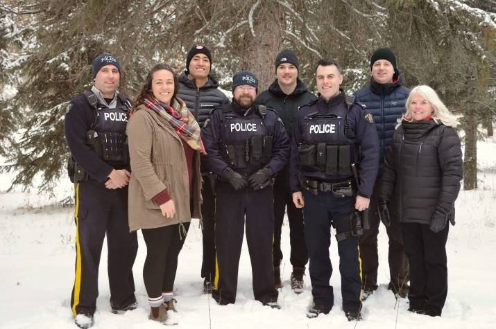 Eight RCMP employees, some wearing police uniforms, stand outdoors in the snow smiling.