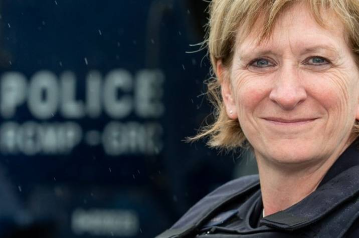 Female police officer standing in front of an armoured vehicle.