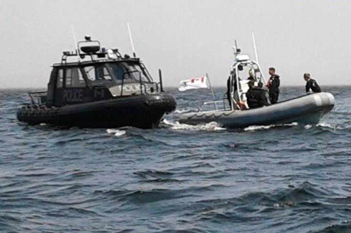 Police officers on a boat next to another boat in the ocean.