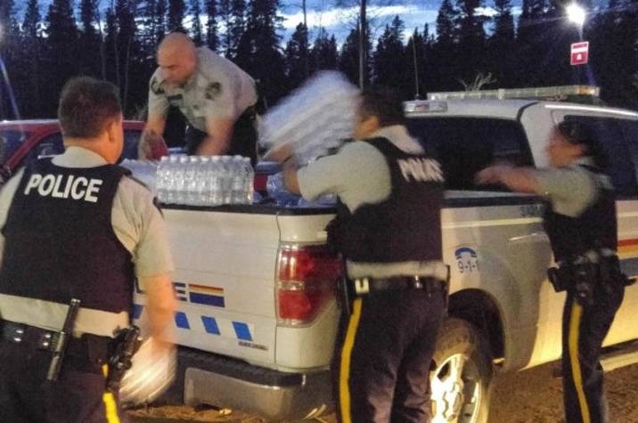 RCMP officers lift packs of water bottles off of a truck.