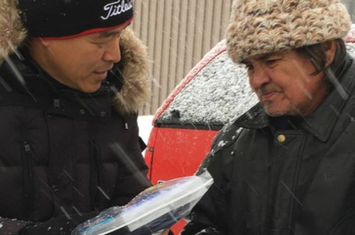 Man offering care package to a homeless man in a snowstorm.