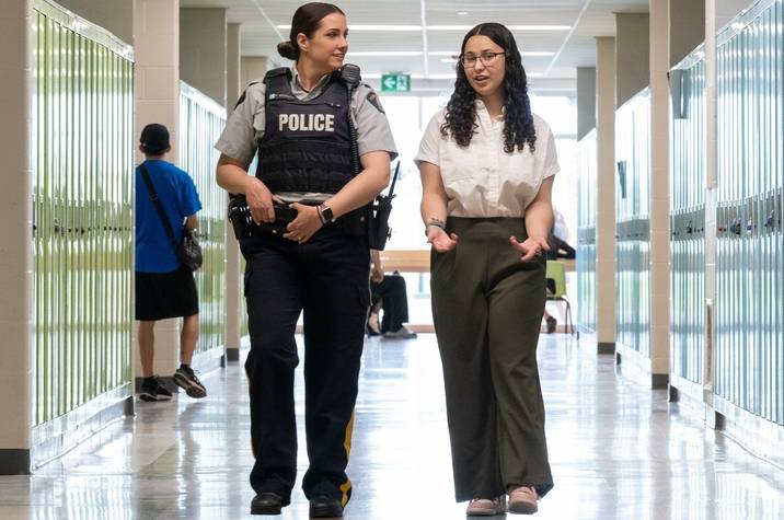A female RCMP officer and a teenage girl walk side-by-side down a school hallway.