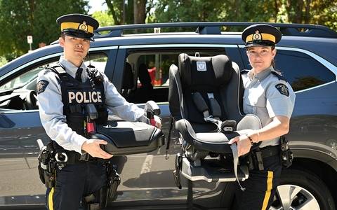 Burnaby RCMP officers holding a booster seat and a car seat