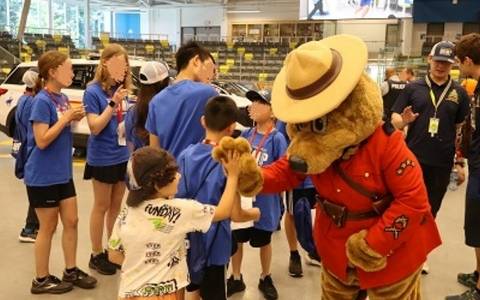 Safety Bear gives a child a high five while surrounded by lots of people at a Coquitlam RCMP event.