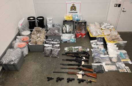 The photo shows drugs including fentanyl and MDMA pills in clear plastic bags, and in grey containers. Eleven firearms, including some black-coloured hand guns are also in the photo.