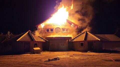 The Mushuau Innu First Nation Band Council Office seen at night with flames emerging from the roof of the structure. Smoke and embers are seen billowing from the fire.
