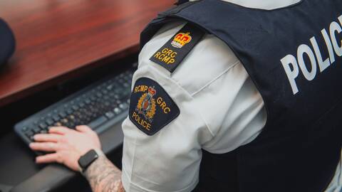 A uniformed RCMP officer sits at a computer, typing.