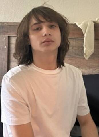 Image of Kaden Platt with shoulder length brown hair wearing a white t-shirt.