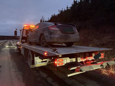 A black passenger car is loaded onto the back of a tow truck.