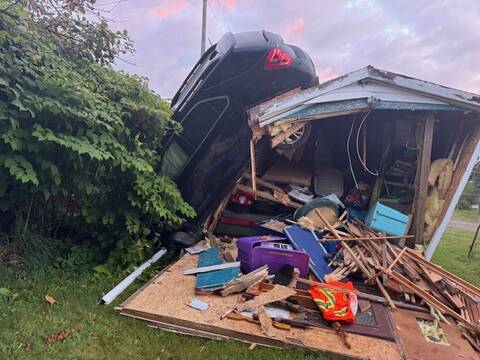 The SUV’s rear tires are on the roof of the shed, and its front bumper rests on the ground. The whole rear wall of the shed is collapsed and the damaged contents of the shed are strewn all over.