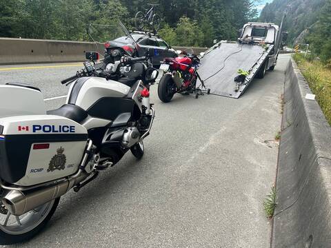 A red sport motorcycle is loaded onto a tow truck on Highway #99 as a BC Highway Patrol motorcycle is parked in the foreground