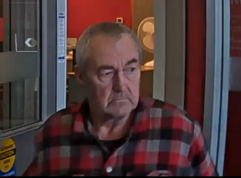 A man in a red and grey plaid shirt exiting a bank.