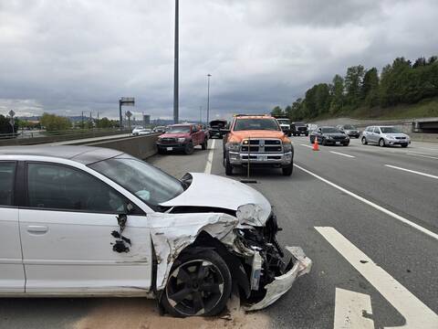 A heavily damaged white Audi that is about to be towed away. A damaged red Toyota pickup and a black Chevrolet police SUV are in the background