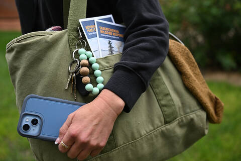 A person holding a shoulder bag and cell phone. One French and one English wildfire resource pamphlet are in the front pocket.