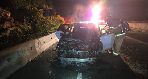 Photo of a Toyota Prius smouldering on the side of the highway, with a fire fighter tending to the car.