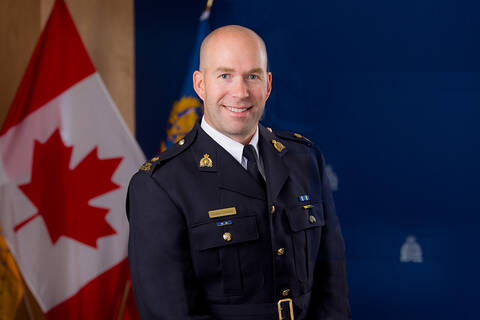 Supt. Chris Goebel smiles indoors in front of a blue background and a Canada Flag