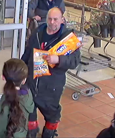 Surveillance photo of an unknown male suspect in a Grand Falls-Windsor retail theft investigation, carrying groceries and a case of soda near a store entrance