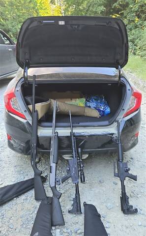 Photo of 4 guns leaning up against the back of a black Honda Civic.
