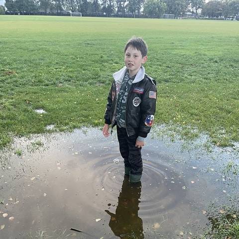 A young boy with brown hair, standing in a puddle.