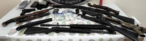 Firearms, cash and small bags of drugs displayed on a table.