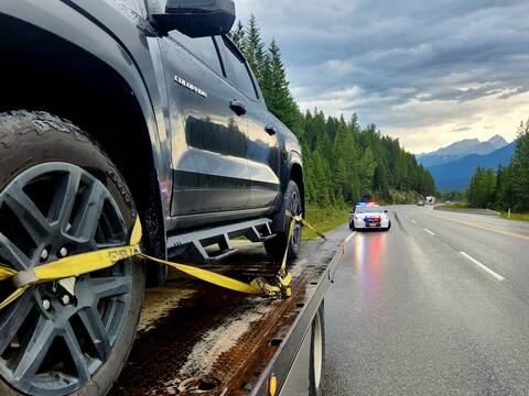 A BC Highway Patrol cruiser stands by as a black truck is secured on a tow truck because of excessive speeding on Highway 93 in Kootenay National Park