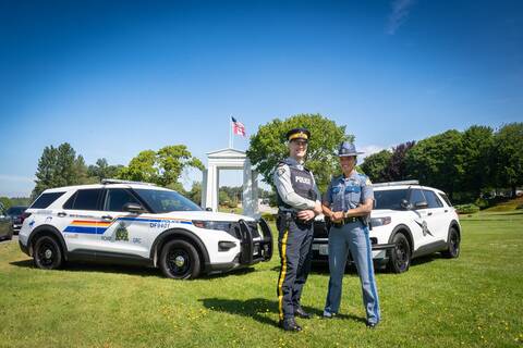 A BC Highway Patrol vehicle and a Washington State Patrol vehicle sit in front of the Peace Arch with a uniformed BCHP officer and WSP trooper