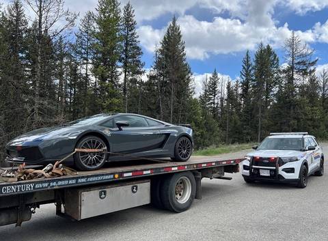 A Lamborghini Gallardo sitting on the back of a tow truck while a BC Highway Patrol cruiser supervises