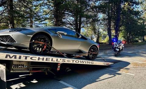 A grey Lamborghini Huaracan on a tow truck behind a BC Highway Patrol motorcycle