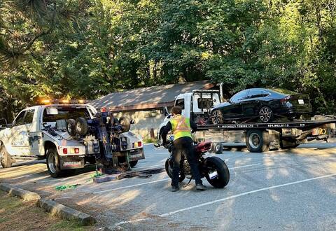 A tow-truck driver prepares an impounded motorcycle for the tow-truck while another impounded vehicle is about to be towed away on the Sea to Sky Highway